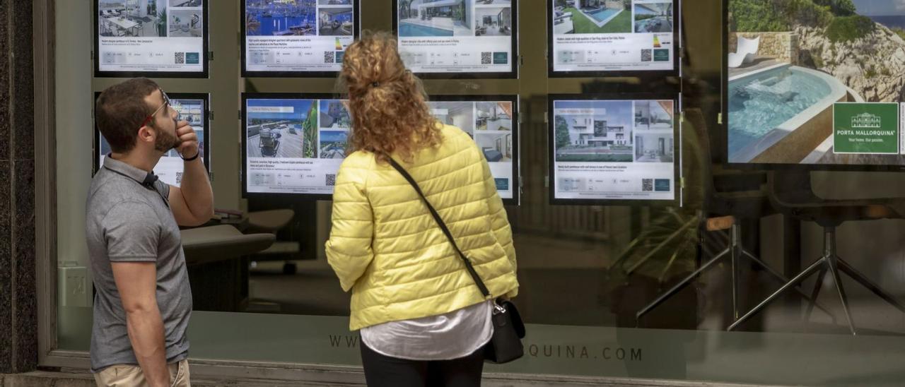 Un hombre y una mujer miran con atención los anuncios de viviendas en el escaparate de una inmobiliaria.
