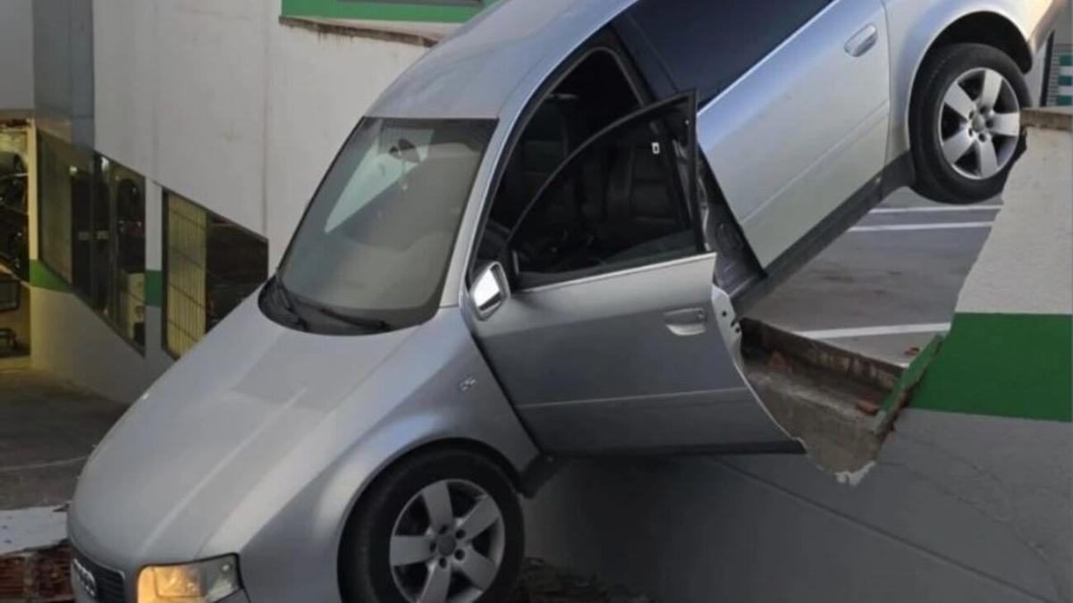 El coche después de traspasar el muro de un aparcamiento de un supermercado.