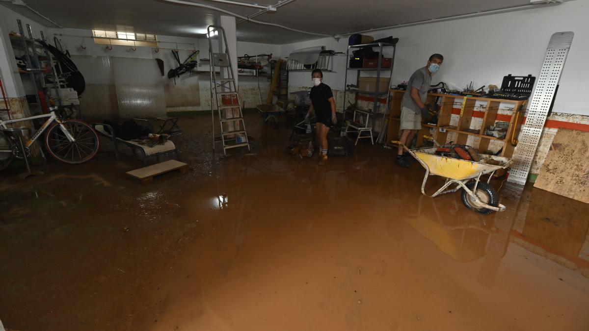 Dos vecinos cargan una carretilla con enseres para tirar de su garaje, en el que llegó a entrar más de un metro de agua.