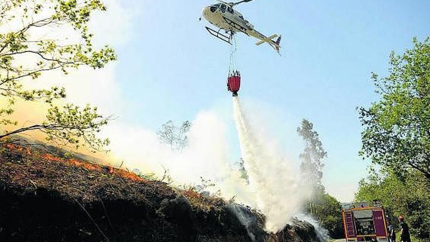 Un helicóptero arroja agua sobre el fuego que corre por la ladera. / bernabé / javier lalín