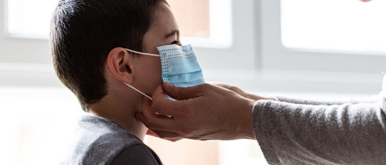 Una madre coloca la mascarilla a su hijo.