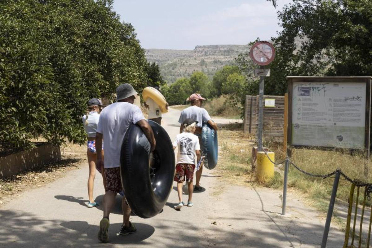 Una familia con flotadores y una barca pasa por el acceso cerrado al área recreativa de l'Esgoletja.