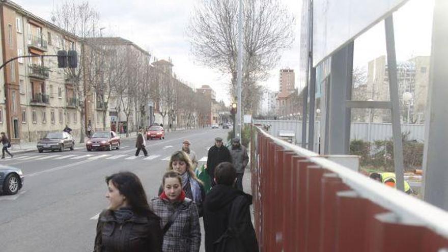 Varios peatones pasan junto a las obras del aparcamiento.