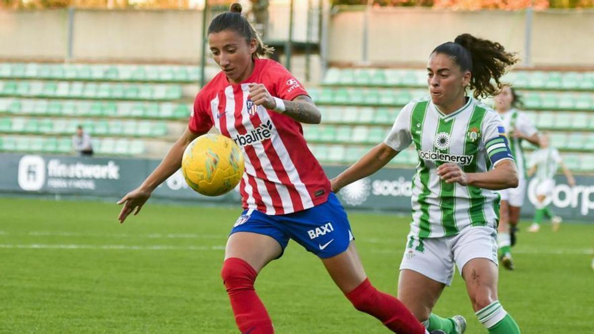 Nana, del Betis, disputa el balón ante Sheila Guijarro, del Atlético, durante un partido de la Liga F. De fondo, las gradas vacías.