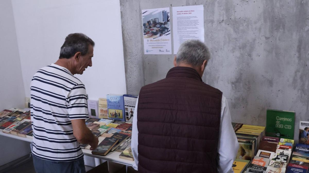 Usuarios ojean los libros del mercadillo, situados en el vestíbulo de acceso.