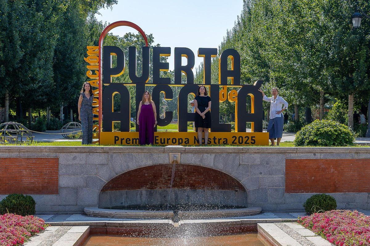 Las responsables de Patrimonio del Ayuntamiento frente al cartel instalado en el Retiro en homneaje al Premio Europa Nostra 2025 recibido por el proyecto de restauración de la Puerta de Alcalá.