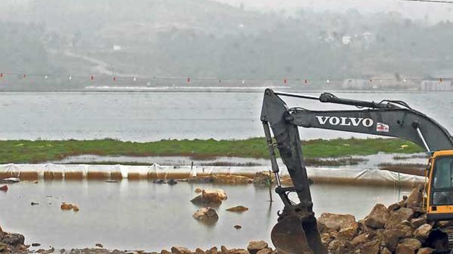 Una pala excavadora prepara el terreno para las obras en la orilla del río Ulla, rodeada por una barrera antiturbidez.  // Iñaki Abella