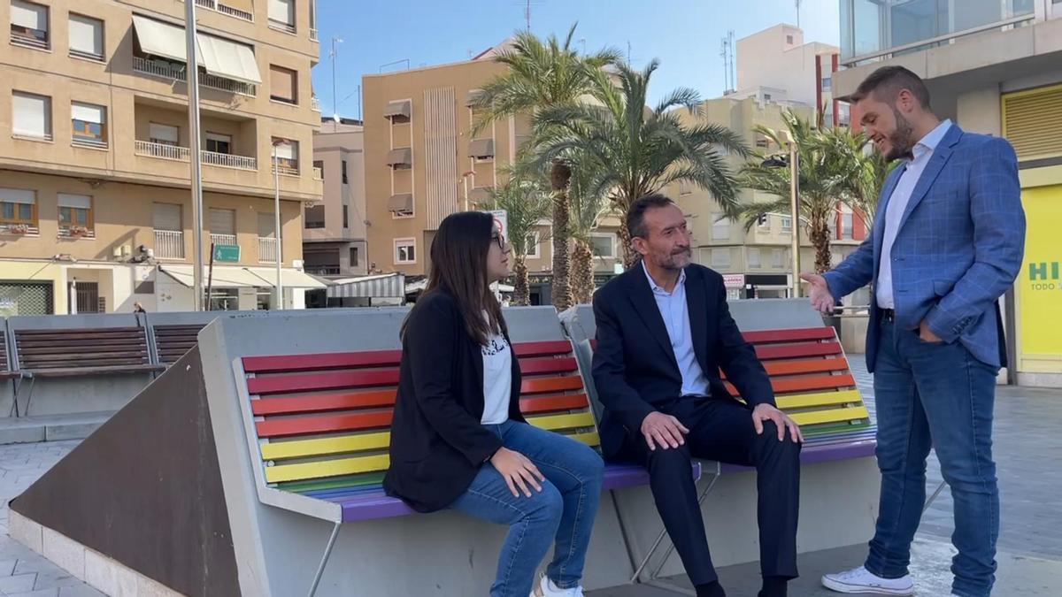 El candidato socialista sentado en un banco de Elche con la bandera arcoíris