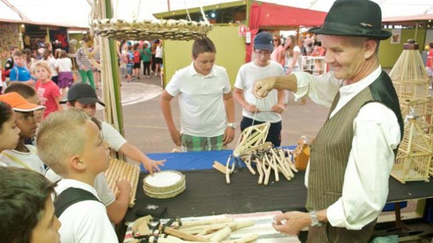 Arriba, un artesano muestra a un grupo de escolares uno de sus artilugios. Debajo,  a la izquierda, varios niños en uno de los stands y a la derecha, la artesana Mari Carmen Cabrera, en el Taller de Calado del Cabildo.  i C. DE SAÁ