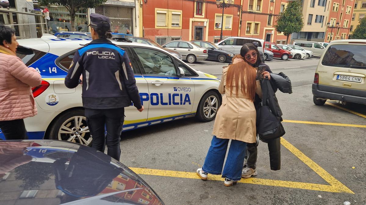 La cuñada y la sobrina de la herida en el incendio de La Tenderina se abrazan junto a un coche policial.