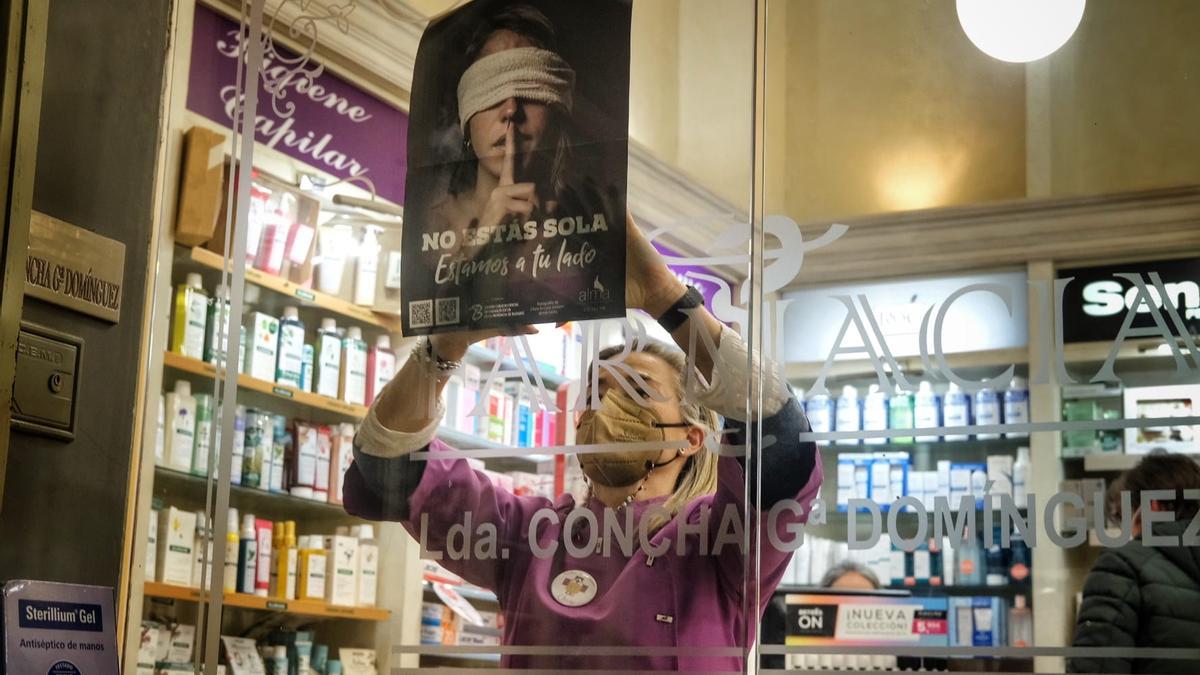 Una trabajadora de una farmacia de Badajoz cuelga el cartel de la campaña.