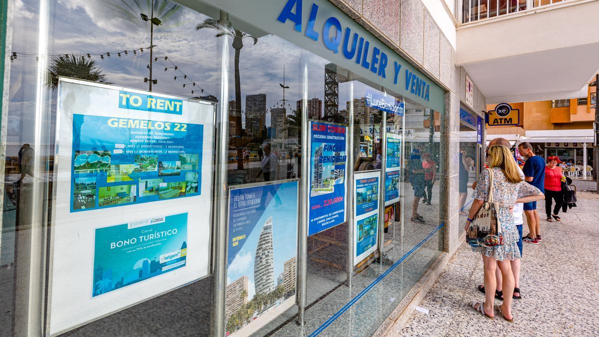 Turistas consultando precios de pisos en la puerta de una inmobiliaria en Benidorm.