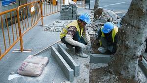 Unos obreros realizan obras en una acera de las calles de Barcelona.