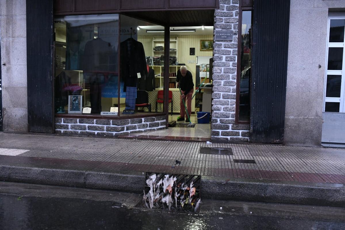 Un comerciante limpia su local antes de iniciar su actividad tras las fuertes lluvias de la mañana de hoy sábado en Pontevedra.