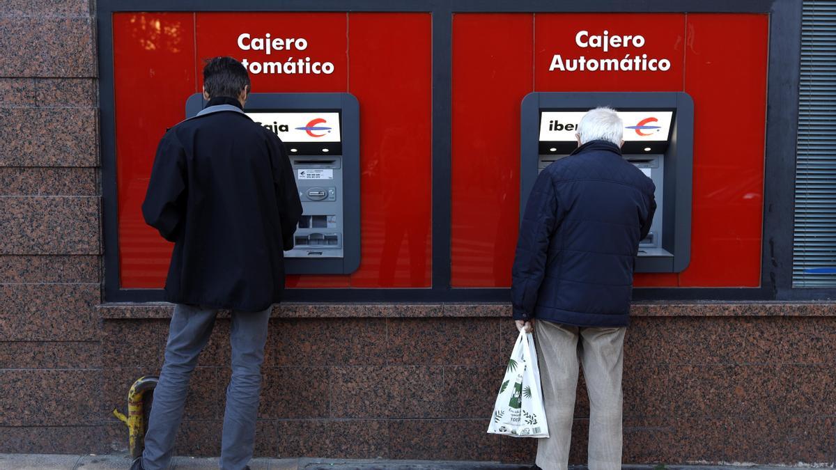Varias personas sacando dinero en cajeros automáticos de Ibercaja en el centro de la ciudad de Zaragoza.