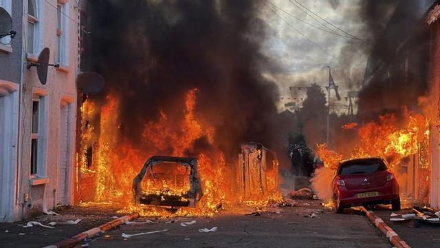 Vehicles en flames a Belfast durant els disturbis per l’apunyalament d’un home en mans d’un sol·licitant d’asil sudanès. | PA WIRE / EUROPA PRESS