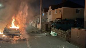 Un coche en llamas en el distrito de Ely, en Cardiff, el 22 de mayo de 2023, por unos disturbios tras la muerte de dos adolescentes en un accidente de tráfico.