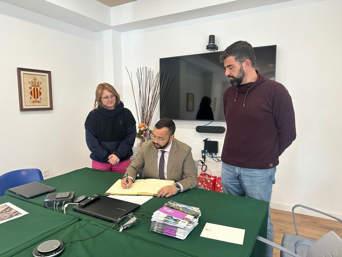 El subdelegado del gobierno, sentado, firma en el libro de honor de Tibi en presencia del alcalde
