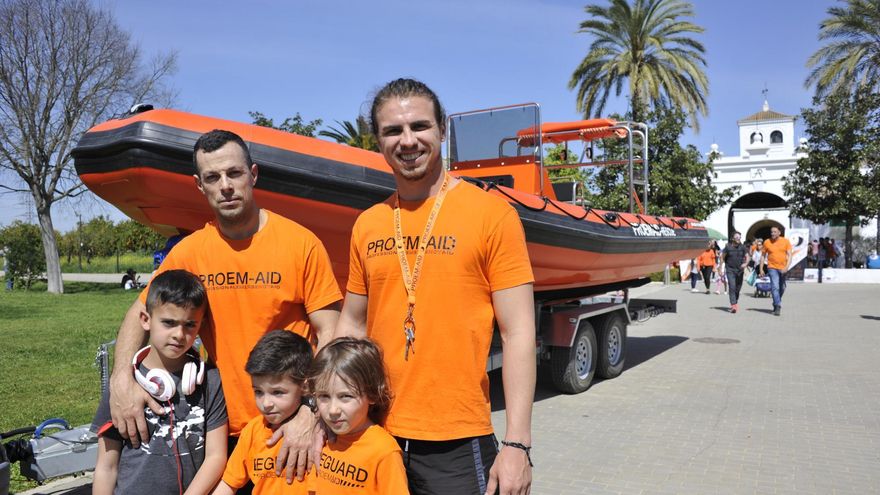 Dos bomberos de Proem-Aid posan con niños asistentes al festival, delante del barco de rescate que hay que terminar de equipar. / El Correo
