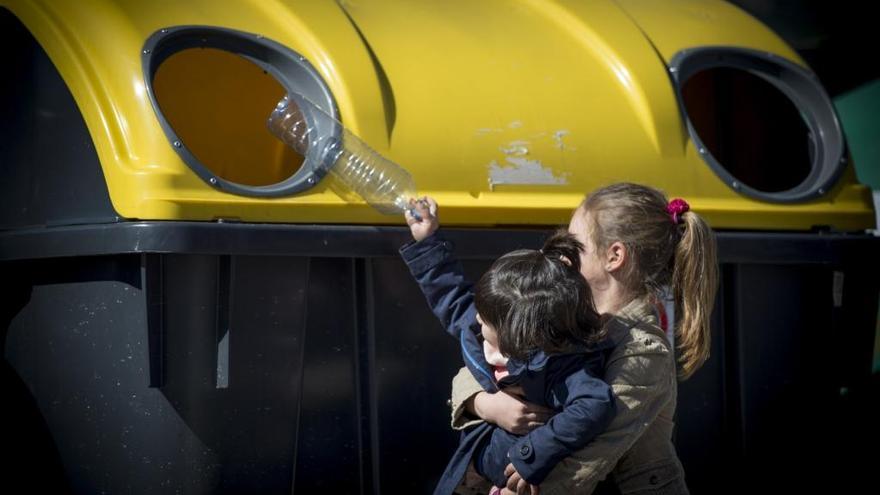 Dos niñas lanzan una botella de plástico al contenedor de reciclaje habilitado para ello: el amarillo.