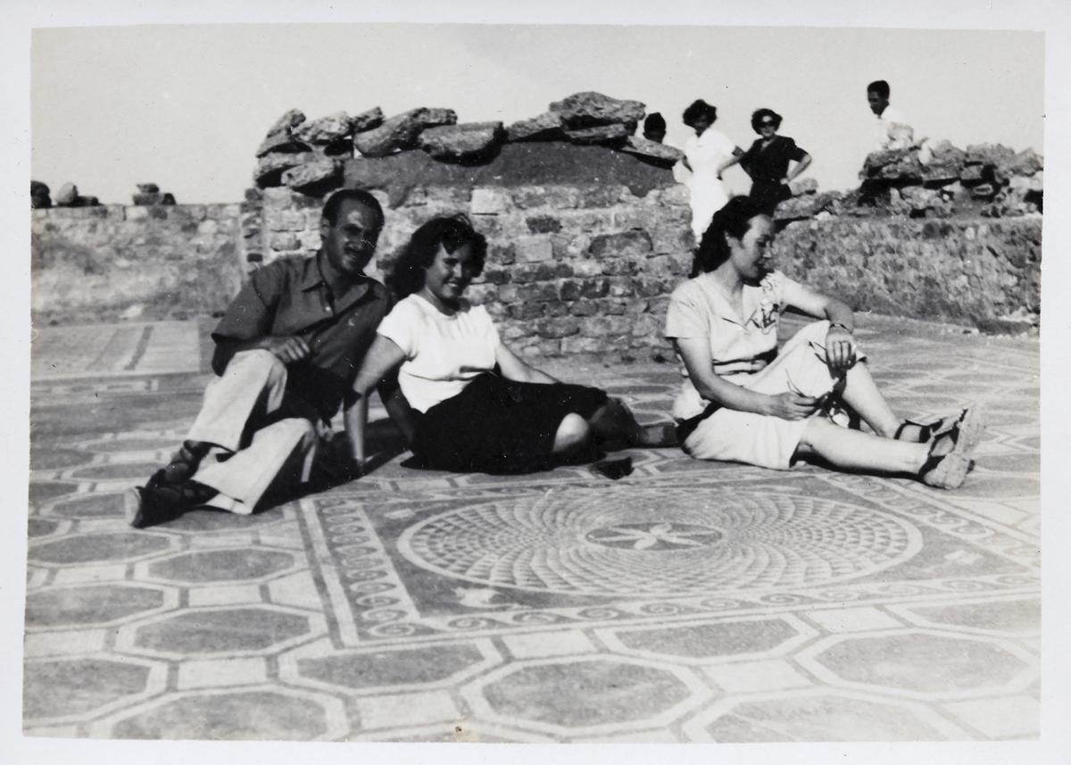 Tres persones assegudes sobre el mosaic dels dofins, un dels més ben elaborats de les ruïnes d’Empúries, quan encara s’hi podia passejar lliurement, també a la dècada de 1930.