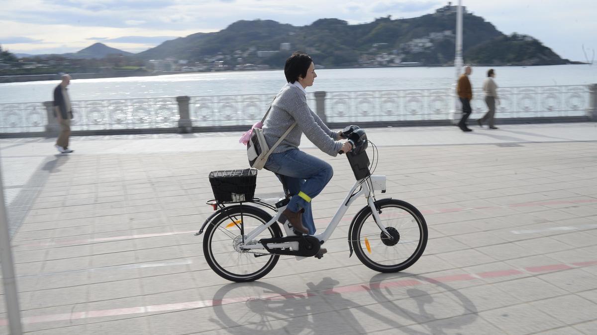 Una mujer circula en bicicleta eléctrica por el paseo de la playa de la Concha, en San Sebastián.