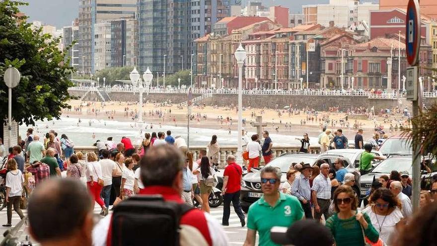 Paseantes en Gijón, el domingo, en la zona del Campo Valdés, con la playa al fondo.