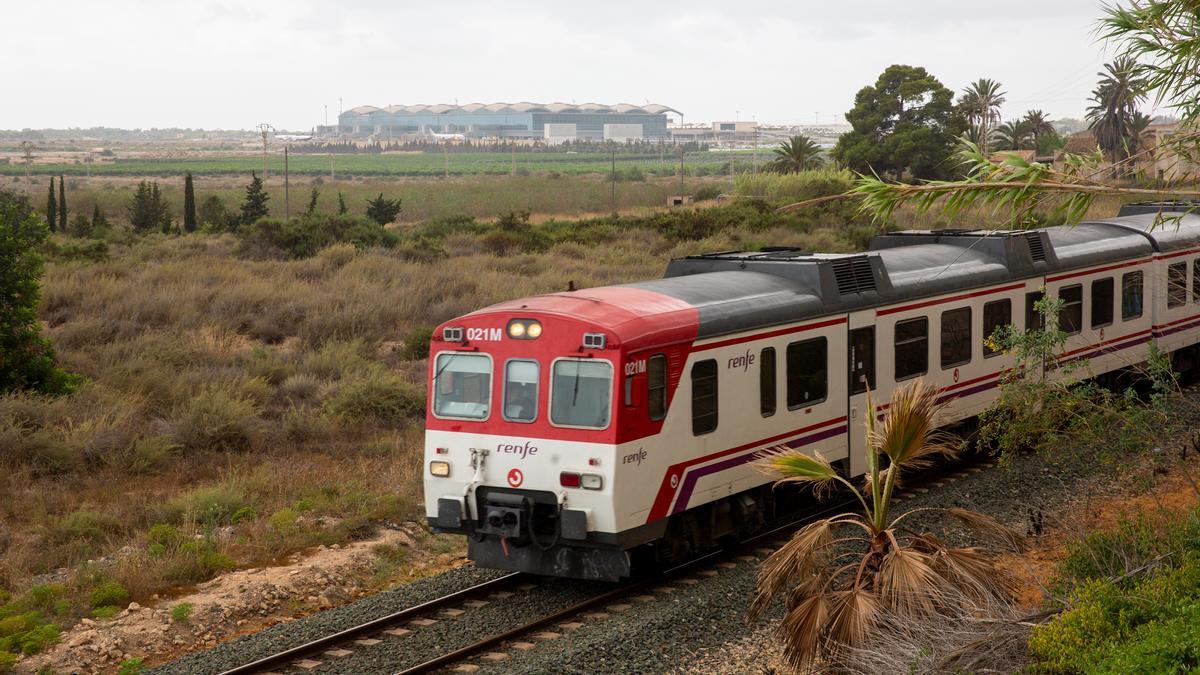 Un tren de cercanías pasa por el actual trazado con el aeropuerto al fondo.