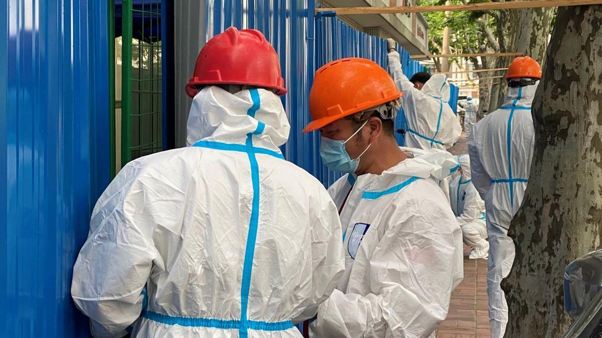 Trabajadores con trajes protectores instalan barreras fuera de un edificio, en Shanghái.