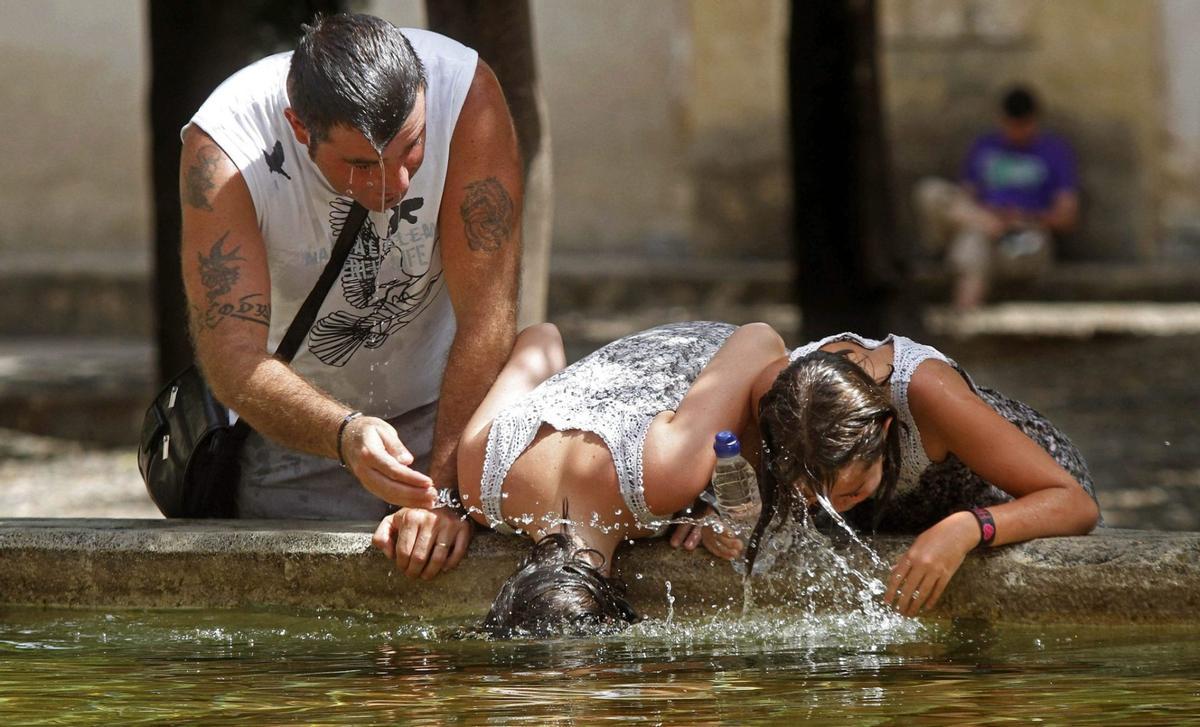 Varias personas se refrescan del calor en una fuente.