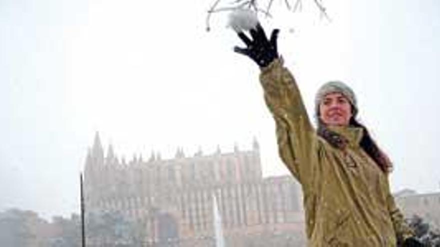 Una joven lanza una bola de nieve con la catedral de Mallorca nevada de fondo.