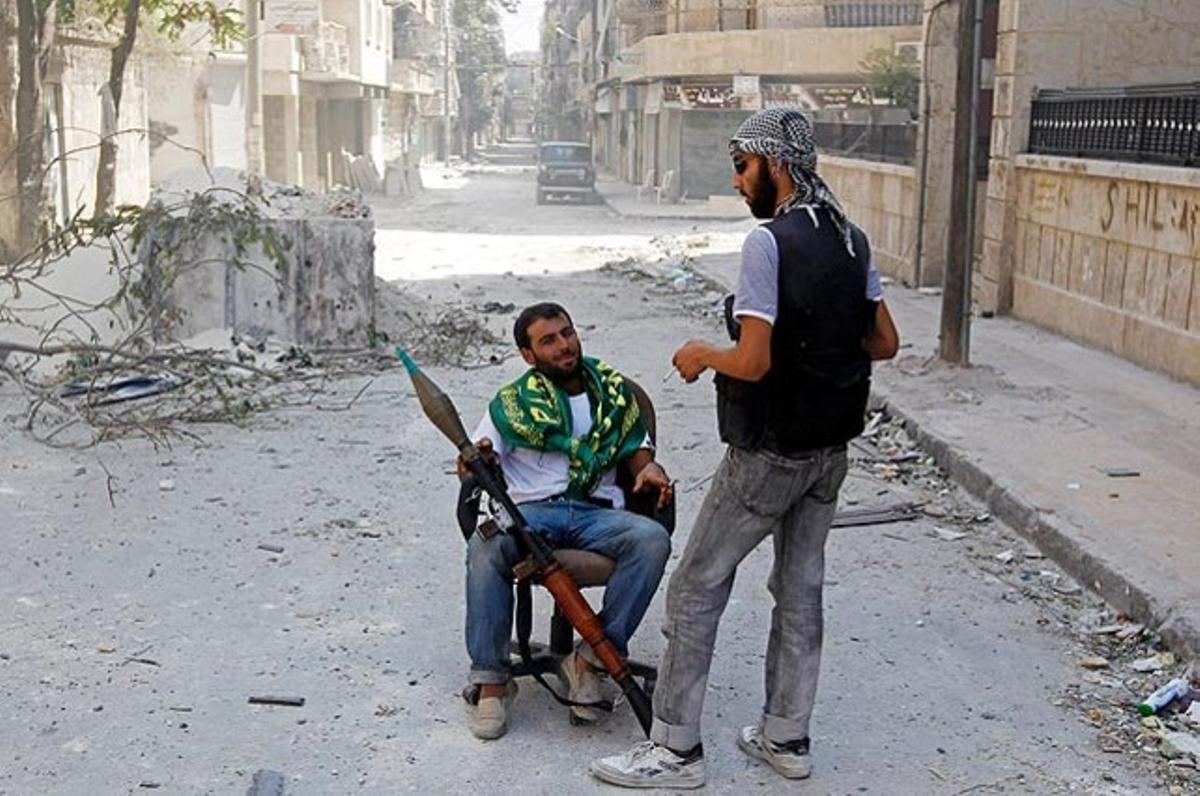 Un guerriller sirià sosté una arma mentre parla amb un altre rebel en un carrer del barri d’Alep.