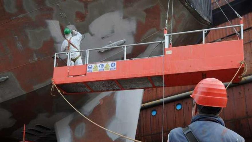 Dos trabajadores pintan un barco en un astillero gallego.