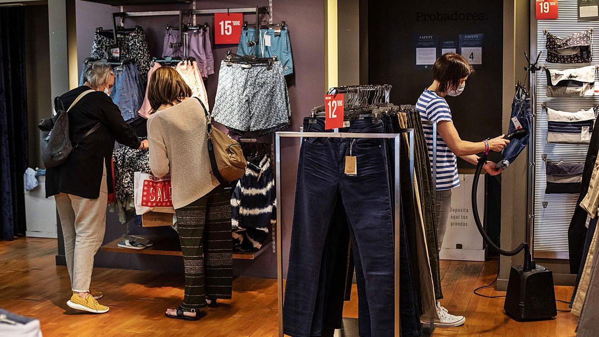 Dos mujeres mirando ropa mientras la dependienta desinfecta un pantalón. | Emilio Fraile