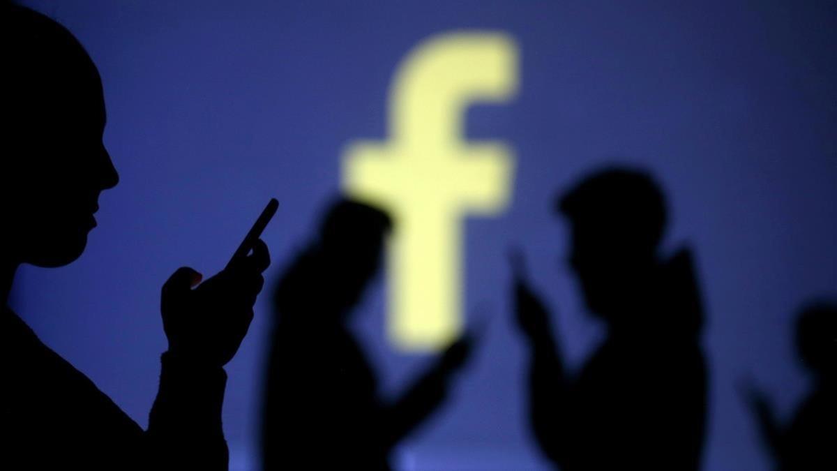 Unos usuarios de Facebook, ante el logotipo de la red social.