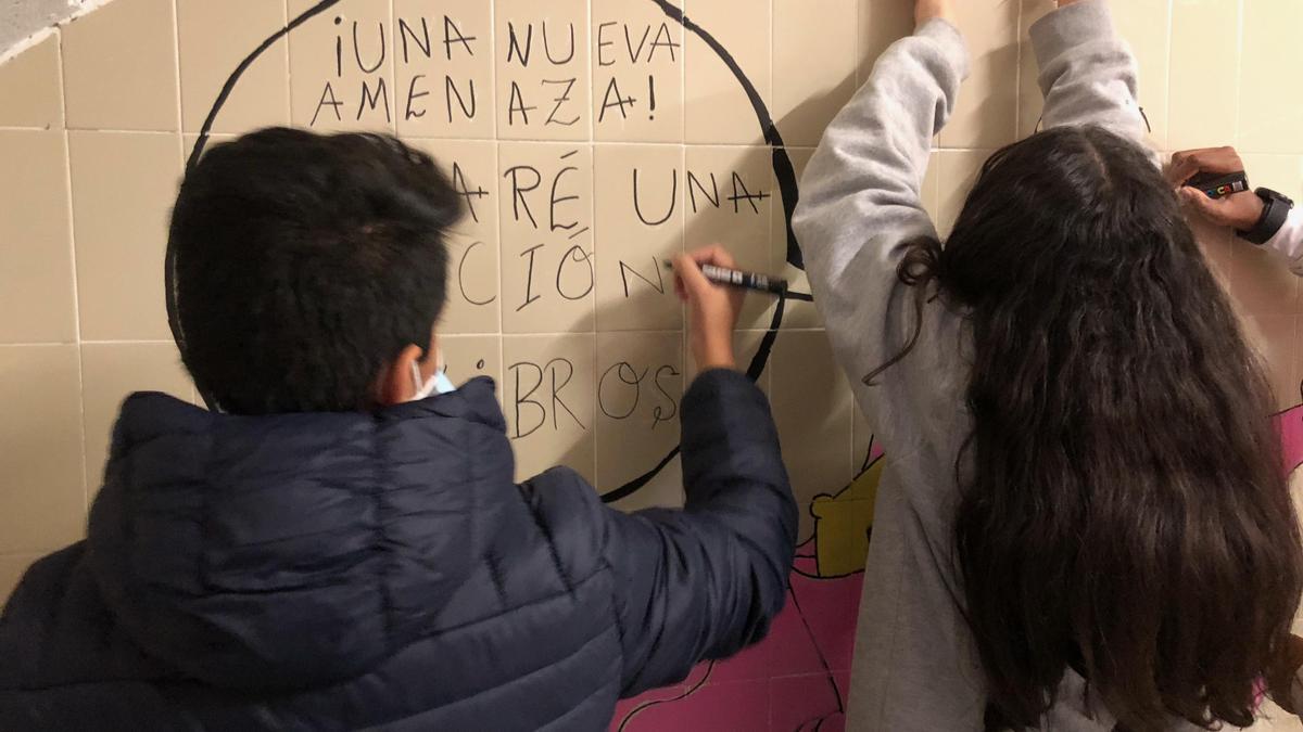 Dos alumnos del instituto zaragozano pintan con rotulador el mural que decora el nuevo espacio de lectura del centro.
