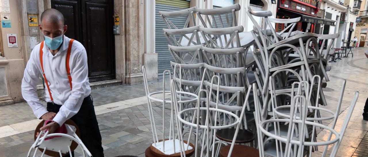 Un empleado recoge la terraza de un local del centro de Málaga.