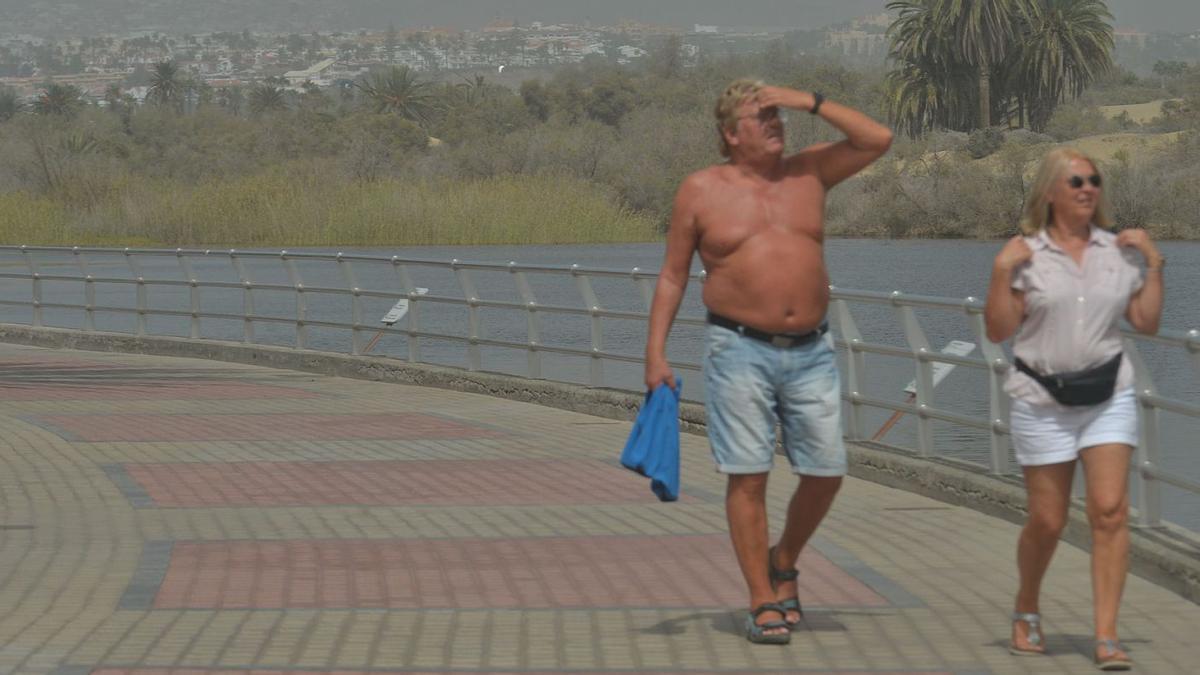 Dos turistas caminan junto a la charca de Maspalomas en un día de octubre con calima. | | JUAN CASTRO