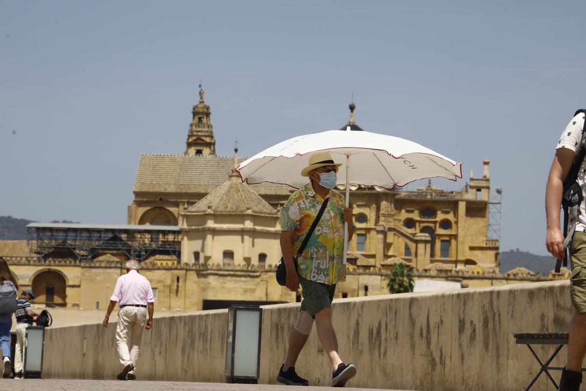 Una persona se protege con una sombrilla del intenso calor mientras pasea este jueves por el puente romano de Córdoba.