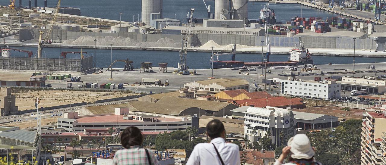 Unos turistas observan los muelles donde se mueve el granel en el puerto de Alicante, pegados a la zona prevista para el gran centro de congresos. | ALEX DOMÍNGUEZ