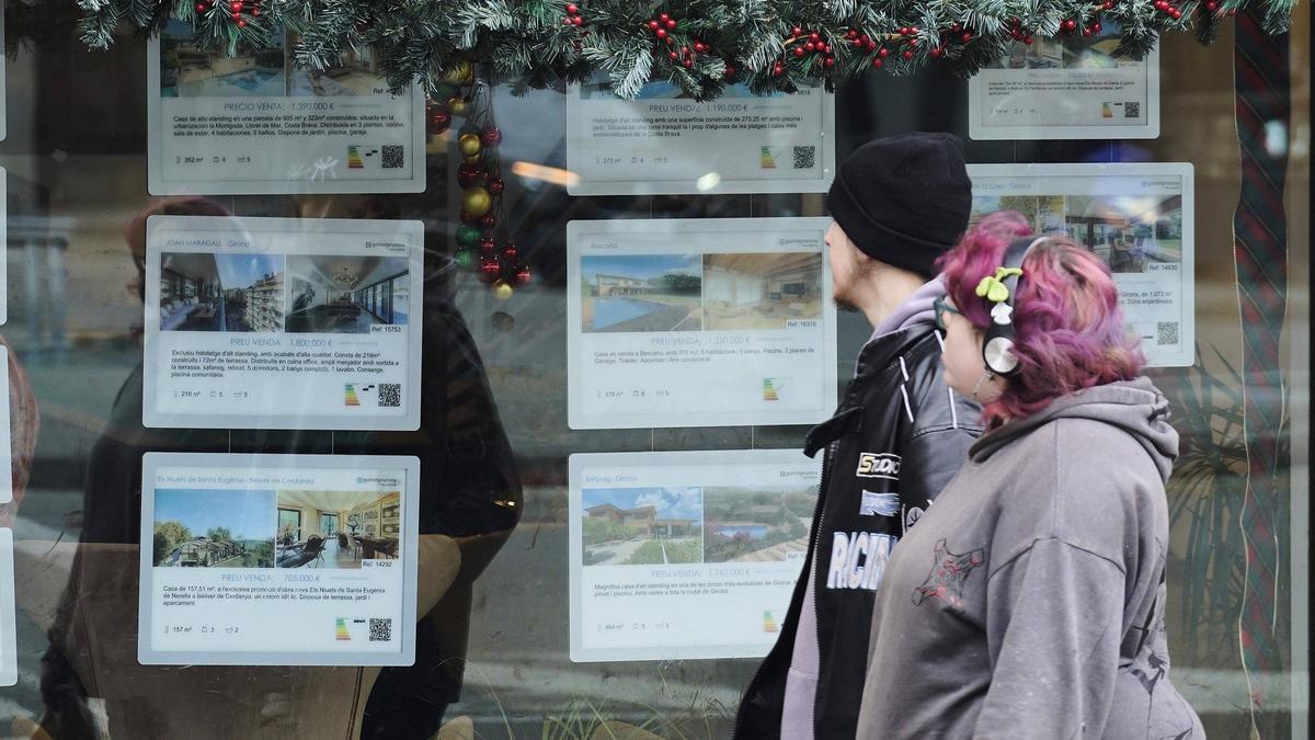 Dues persones davant l'aparador d'una immobiliària a Girona.