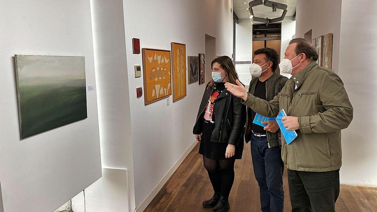 Avelino Mallo explica su cuadro a Pamela Álvarez y Antonio Gil Morán;  a la izquierda, Gil Morán, junto a sus dos obras. | Vivas