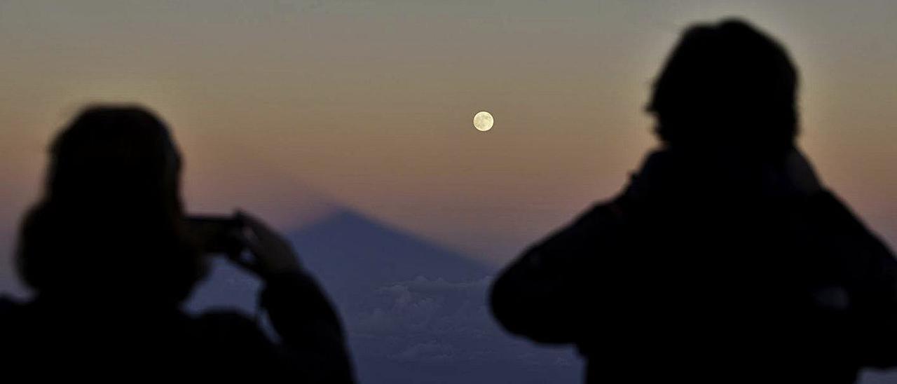 Dos personas observan la luna llena desde el Teide.