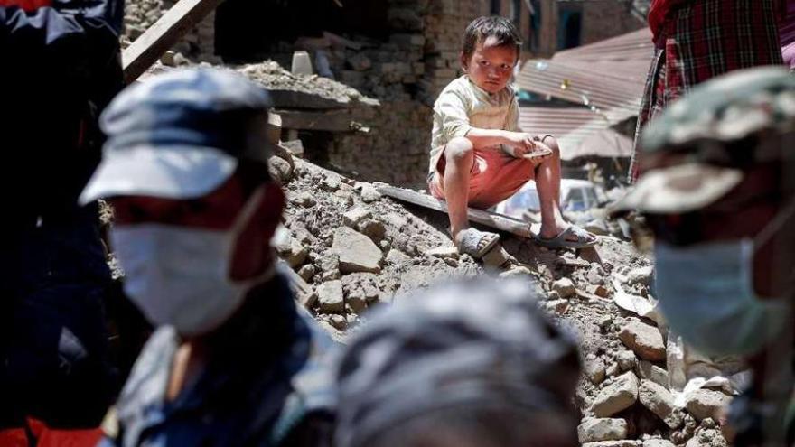 Un niño sentado sobre los escombros observa las labores de los equipos de rescate. // Efe