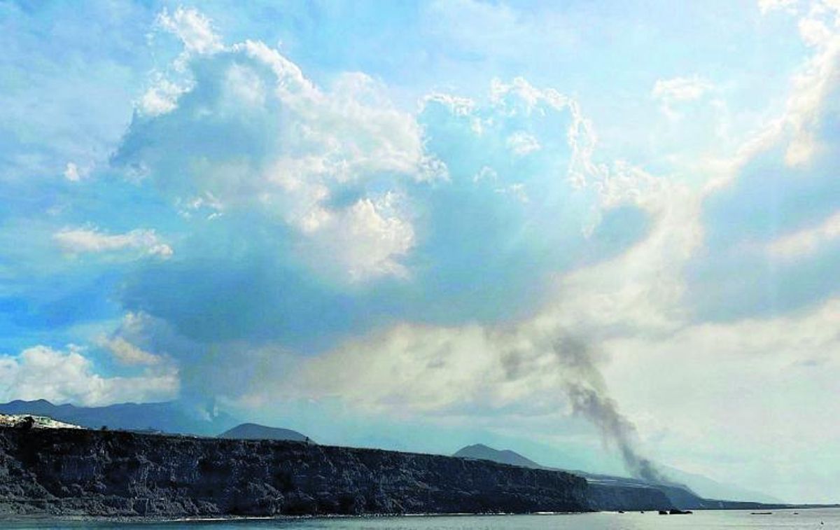 Vista del volcán de Cumbre Vieja a la izquierda de la imagen, con la fumarola negra de la lava que llega a la playa de Los Guirres desde el puerto de Tazacorte. | | E.D.