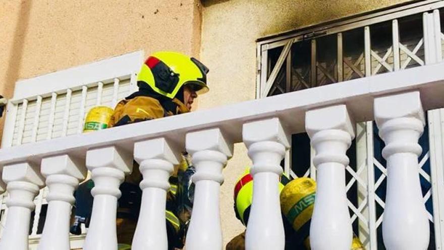 Dos bomberos abren la reja de la casa incendiada en Torrevieja.