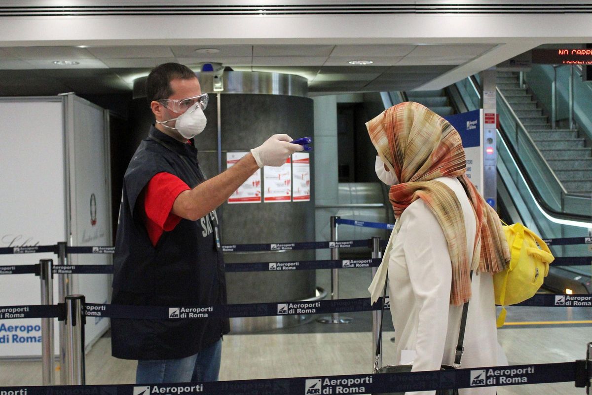 Un vigilante de seguridad toma la temperatura de una viajera en un control en el aeropuerto de Fiumicino de Roma, durante la pandemia.