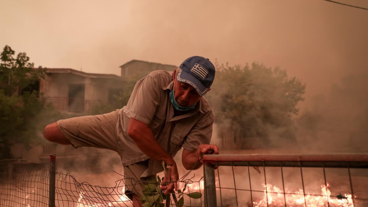 08 August 2021, Greece, Pefki: A man climbs over a fence to escape the flames during a wildfire at Pefki village on Evia island, about 189 kilometers north of Athens. Photo: Pefki/Eurokinissi via ZUMA Press Wire/dpa