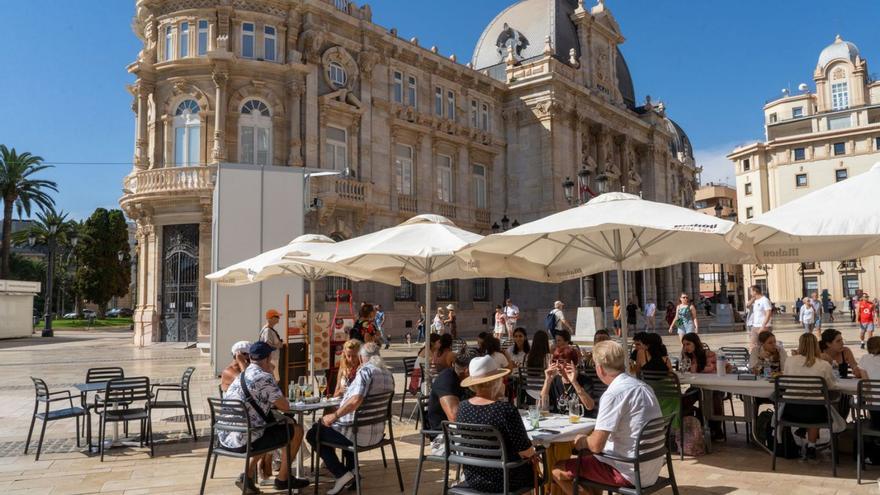 Unos turistas disfrutan del buen tiempo en la plaza del Ayuntamiento de Cartagena.