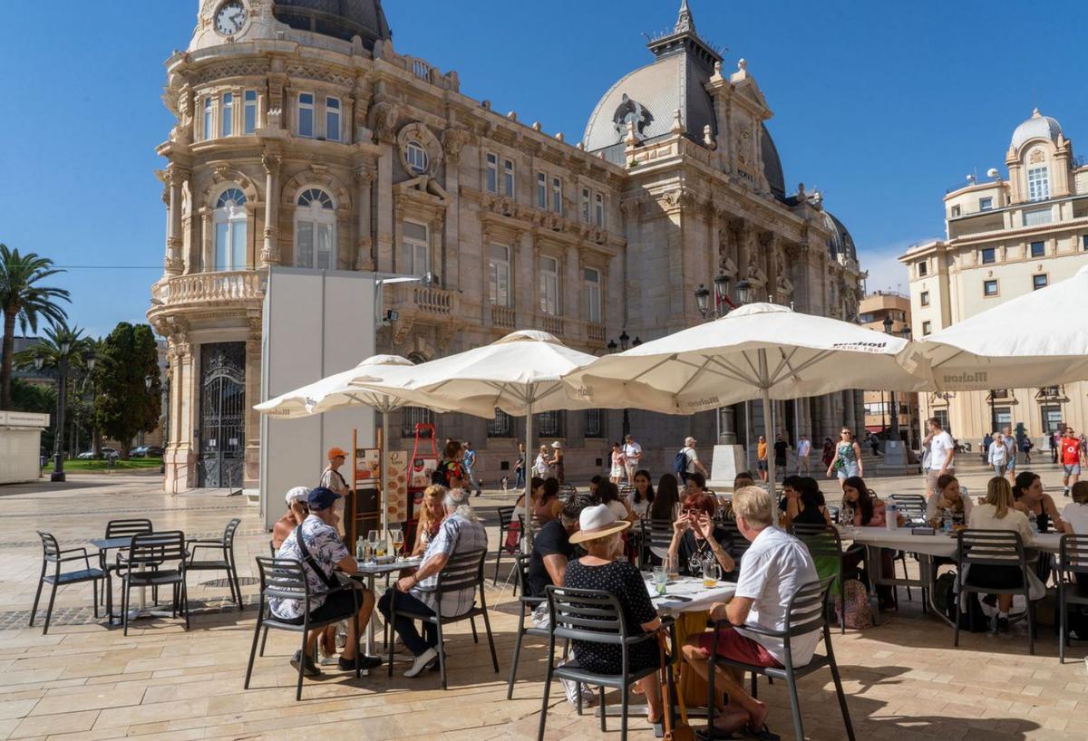 Unos turistas disfrutan del buen tiempo en la plaza del Ayuntamiento de Cartagena.